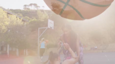 Animation-of-basketball-over-diverse-women-playing-basketball-outdoors