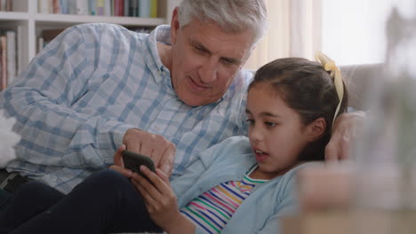 Abuelo-Mostrando-A-Una-Linda-Niña-Cómo-Usar-Un-Teléfono-Inteligente-Enseñando-A-Una-Nieta-Curiosa-Tecnología-Moderna-Niño-Inteligente-Aprendiendo-Teléfono-Móvil-Sentado-Con-El-Abuelo-En-El-Sofá