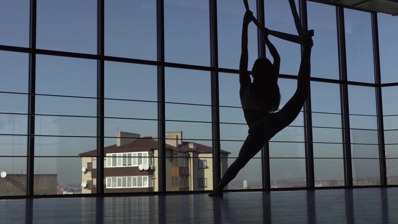 Uomo felice e in forma, vestito con una tuta nera aderente, che pratica fly yoga con un'amaca rossa nel parco, all'interno dei pilastri bianchi coperti.