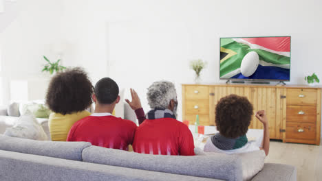 biracial family watching tv with rugby ball on flag of south africa on screen