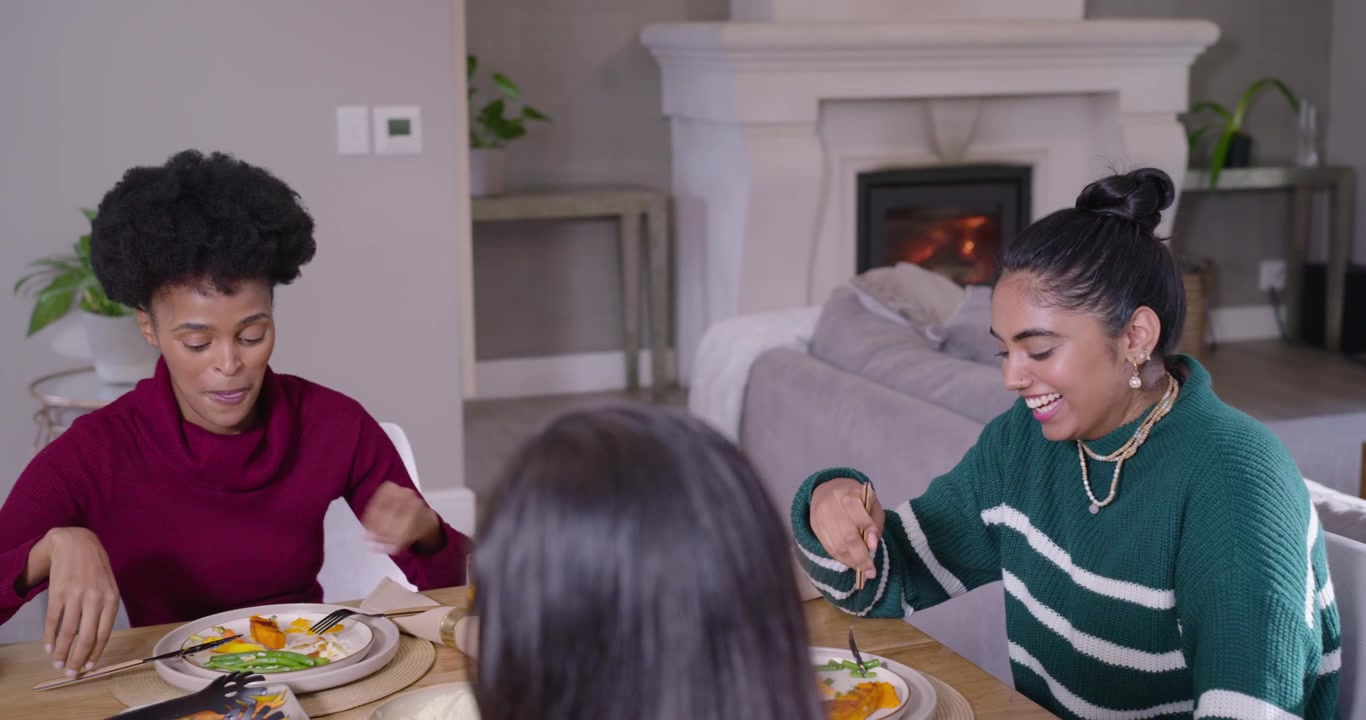 Diverse women friends laughing, eating at table as maroon sweater woman starting remark with forks
