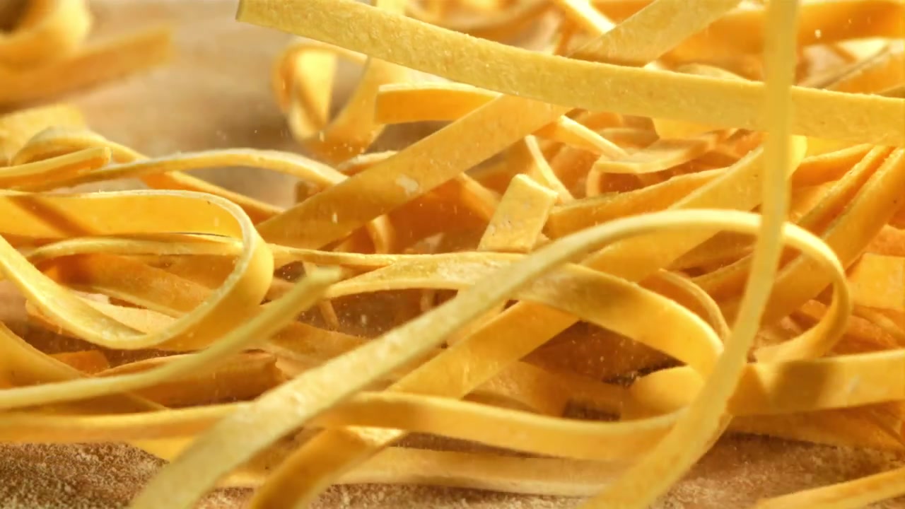 Tagliatelle fresche che cadono su un tavolo di legno infarinato al rallentatore