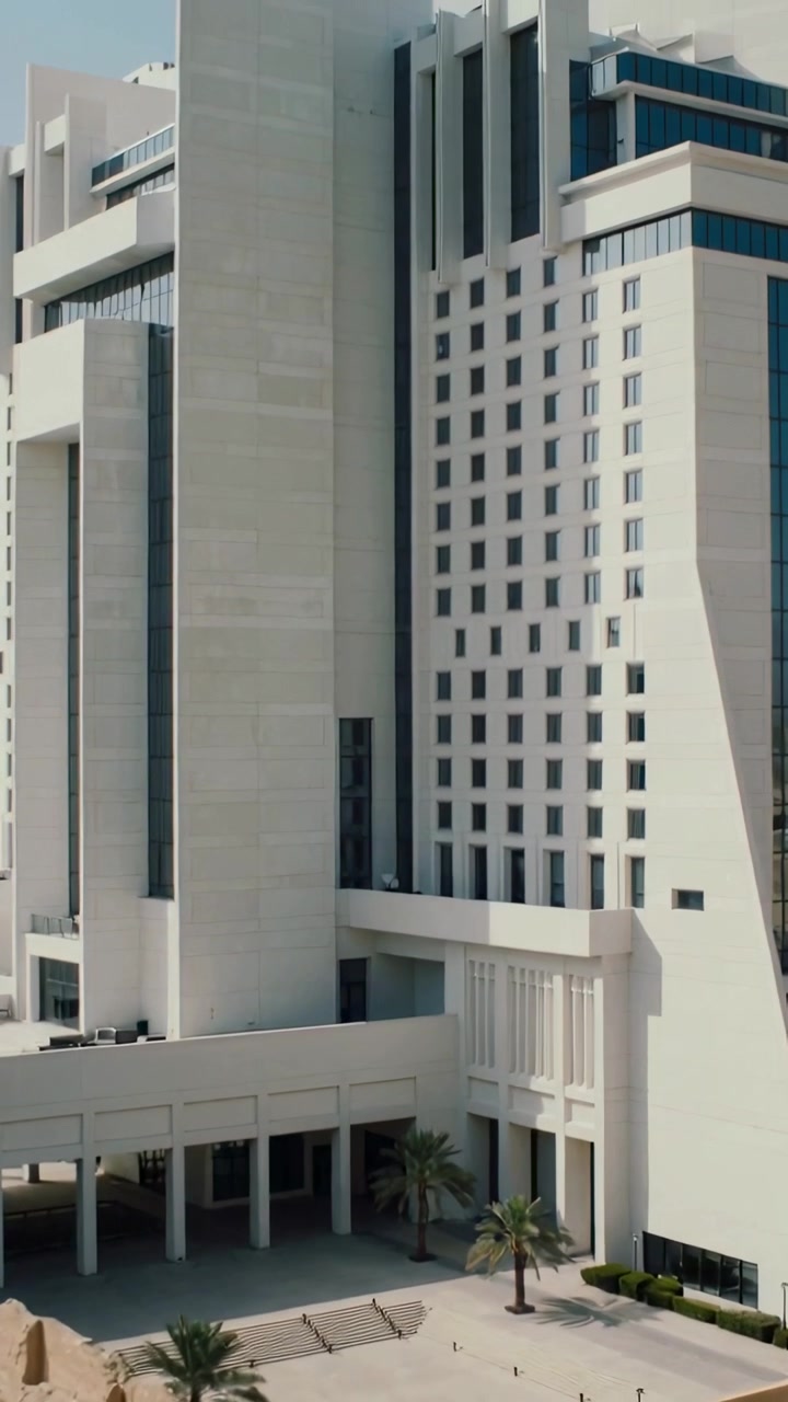 Video vertical: Cámara panorámica revelando edificio beige en la plaza para mostrar fachada y mástiles en la azotea.