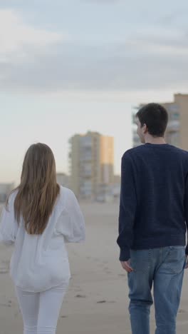 couple walking on a sandy beach with an urban background at dusk