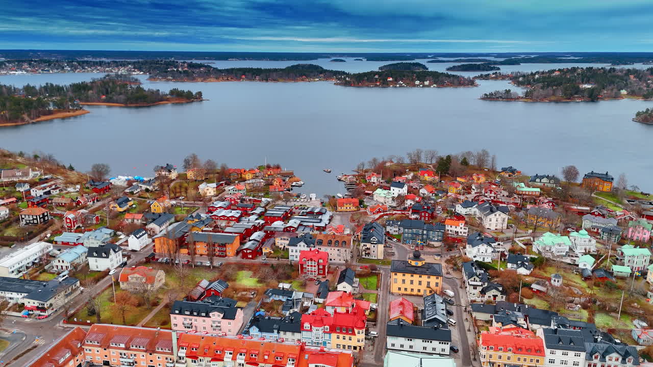 Niedrige, farbenfrohe, schöne Gebäude in der Stadtlandschaft von Vaxholm, Schweden. Mehrere kleine Inseln auf der grauen Wasserfläche des Mälarsees im Hintergrund