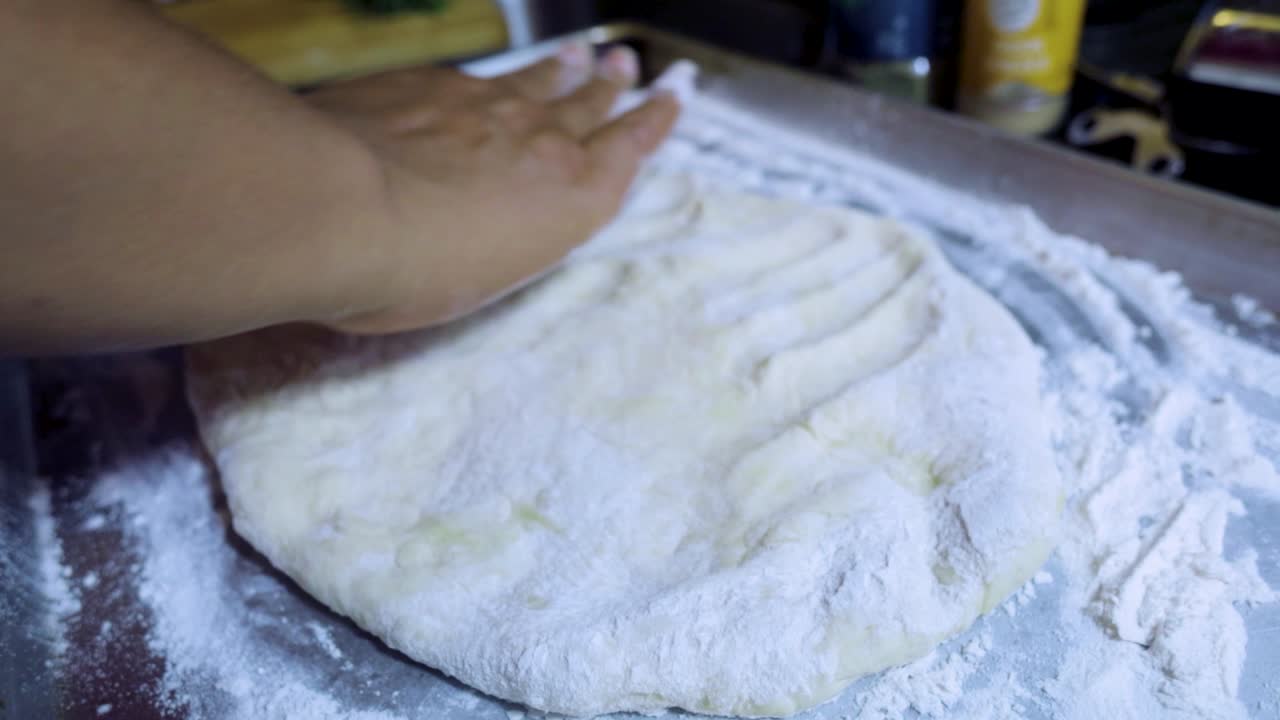 close up view of African american woman's hands kneading pizza dough in a silver pan in slow motion