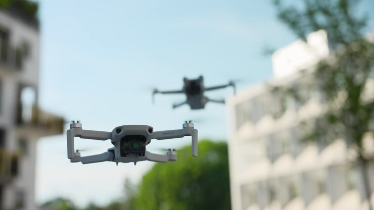 Mini drones quadricópteros voando no ar com paisagem urbana ao fundo.