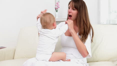 Woman-sitting-on-the-sofa-and-playing-with-baby-in-her-legs