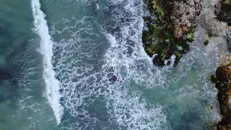 Top-down-drone-view-of-turquoise-waves-breaking-on-rocky-shore