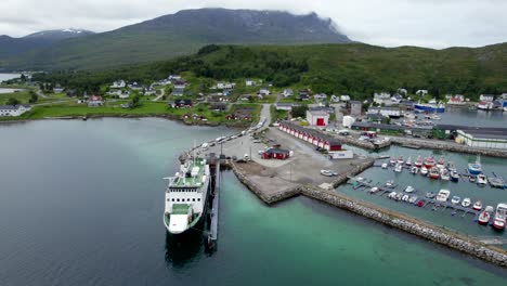 aerial dolly forward view of the ferry at the famous town of botnhamn on senja scenic route in summer with green foliage and cloud draped mountains