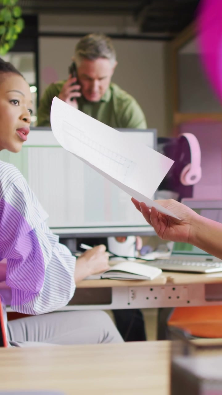 Vertical video: Woman taking paper from right hand for review in office, purple overlay showing doc