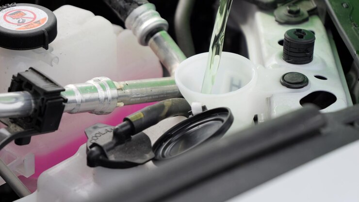 Close detail of a driver topping up windshield washer fluid in a white car during routine maintenance