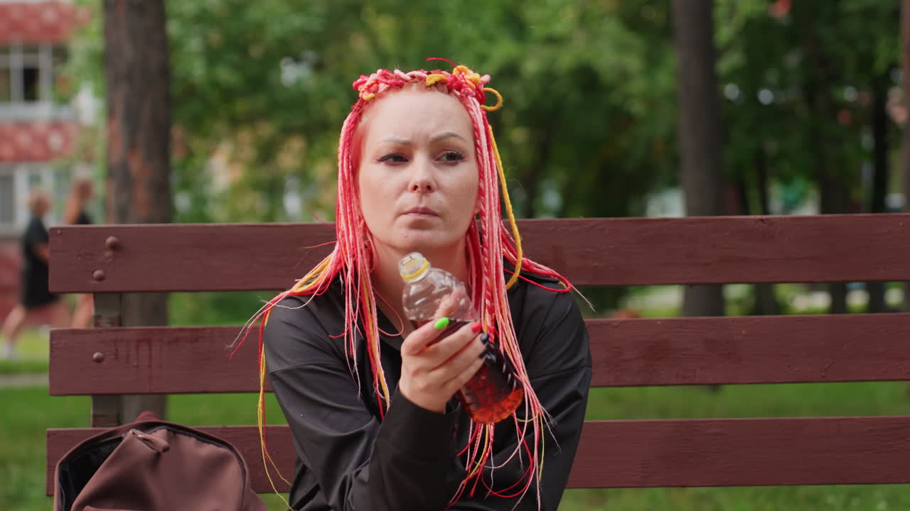 콜라를 마시며 생각에 잠긴 여성의 초상화, 공원에서 소다를 홀짝이는 핑크색 땋은 머리를 한 백인 여성, 핑크색 땋은 머리를 한 여성이 앞을 응시하며 콜라를 편안하게 마시는 도시 공원 풍경