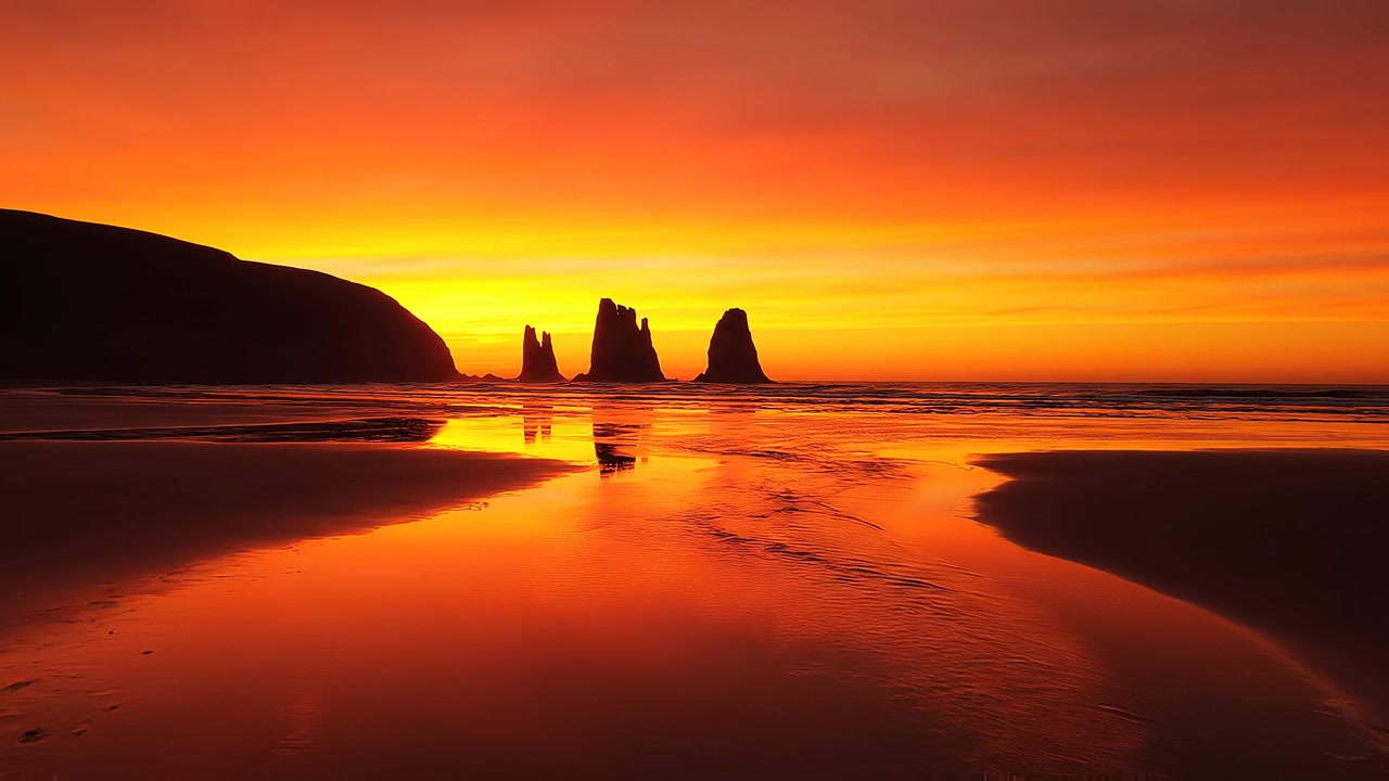 Dramatic orange sunset over sea stacks reflecting on wet sand