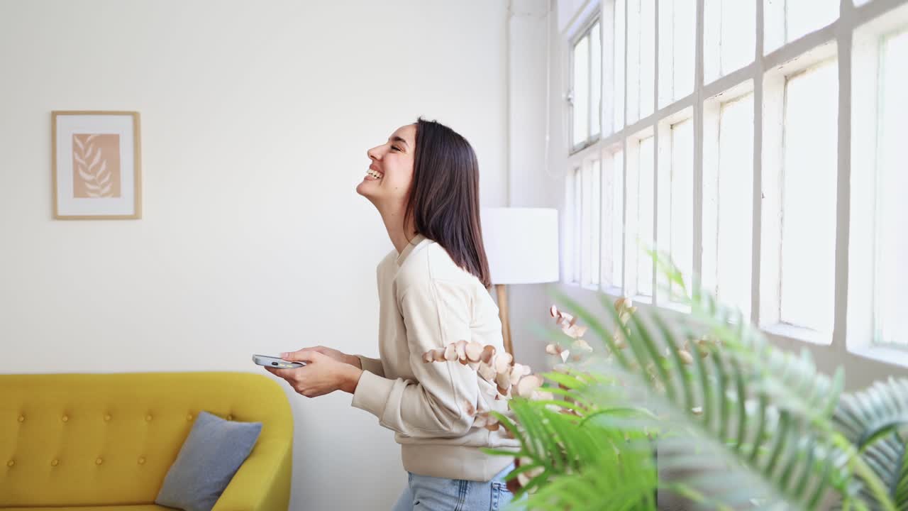 Wanita Muda Tersenyum dan Tertawa Sambil Menggunakan Ponsel Pintar di Rumah