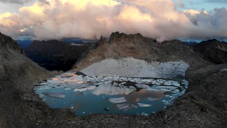 sobrevuelo aéreo hacia un lago lleno de icebergs de un glaciar que se derrite en partes remotas de los alpes suizos con nubes que brillan durante una puesta de sol