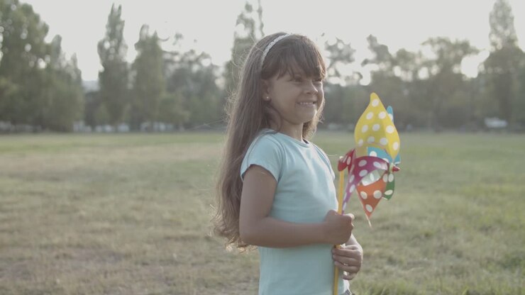 Adorable niña pequeña sosteniendo un abanico de papel en el parque y mirando a su alrededor