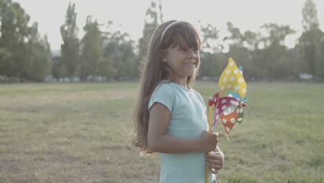 adorable little girl holding a paper fan at the park and looking around