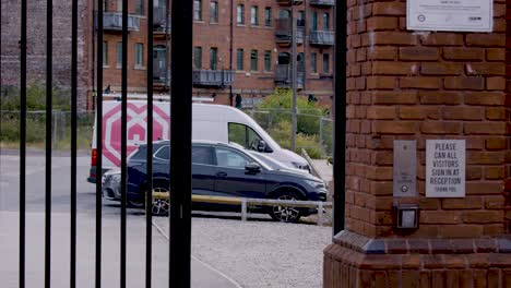 a security gate opens to reveal a parked car and delivery van in a modern urban lot, with steady daylight and static camera framing