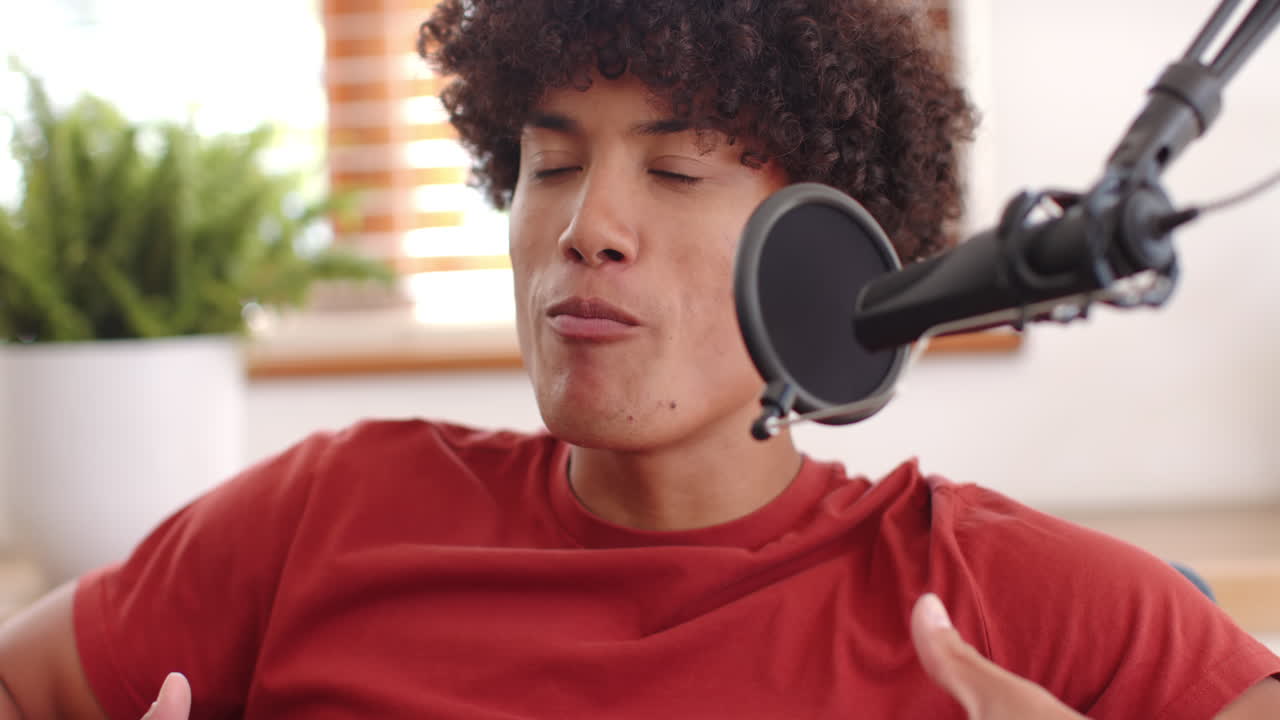 Smiling young man talking into microphone, recording podcast at home