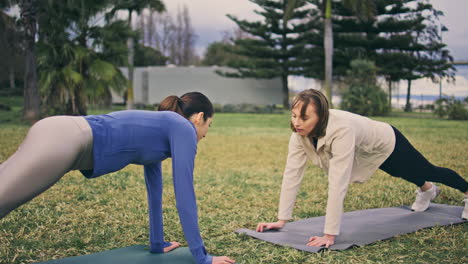 pares deportivos sosteniendo la tabla en el parque. mujeres activas entrenando el cuerpo en el entrenamiento de parejas