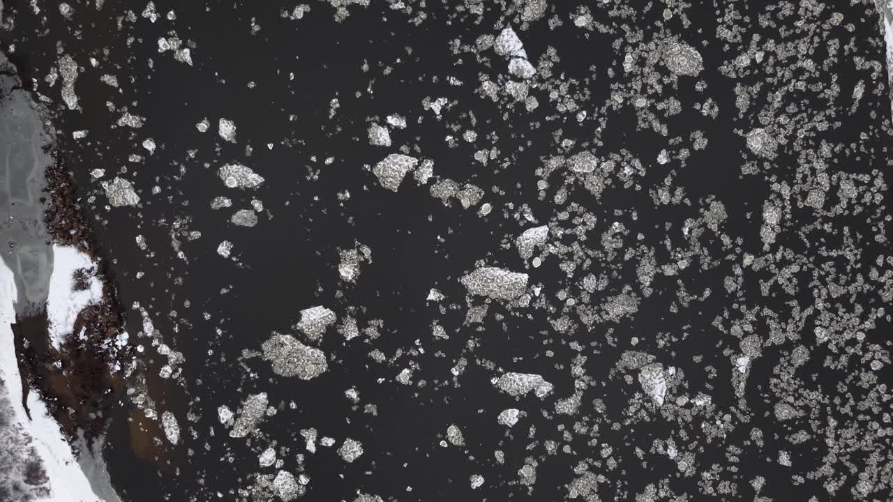 Video di un drone che cattura un'affascinante vista aerea di frammenti di ghiaccio galleggianti su una superficie d'acqua scura. I modelli creano un contrasto sorprendente, migliorando la drammaticità visiva della scena.