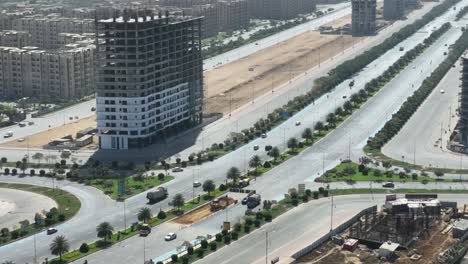 aerial drone shot of cars driving along highway system near a building being constructed in bahria town, karachi, pakistan