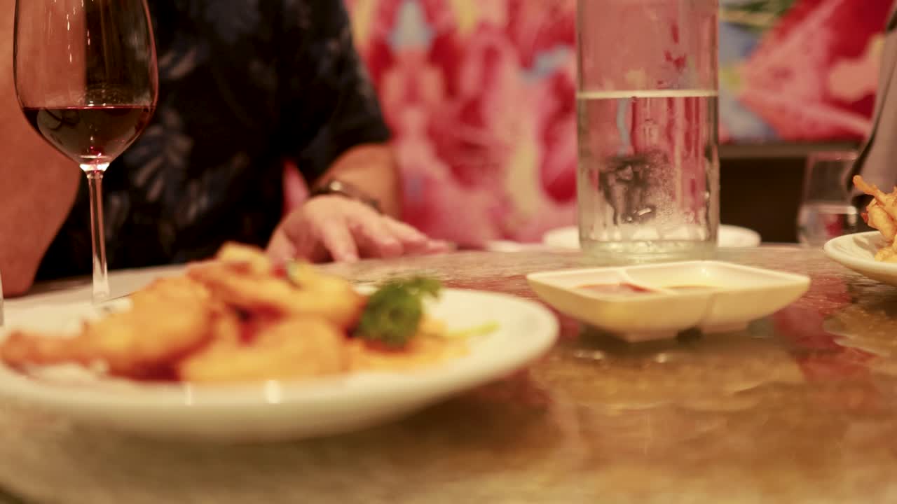 A person rotates a Lazy Susan in a restaurant setting, showcasing a dish and drinks under warm lighting