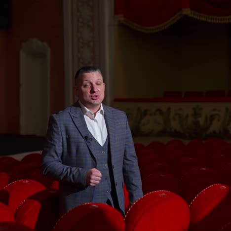 Monologue of an actor in empty theater. Professional performer in suit standing among red chairs in theatrical hall and talking on camera. Pandemic