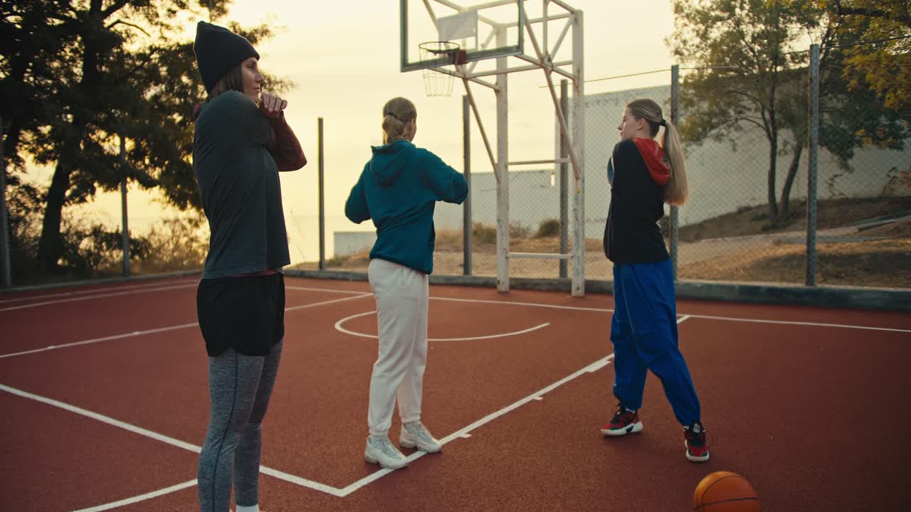 A trio of girls warming up before their basketball practice on the Red Court near an orange basketball on a summer morning. A trio of girls getting ready to play basketball and warming up in the morning