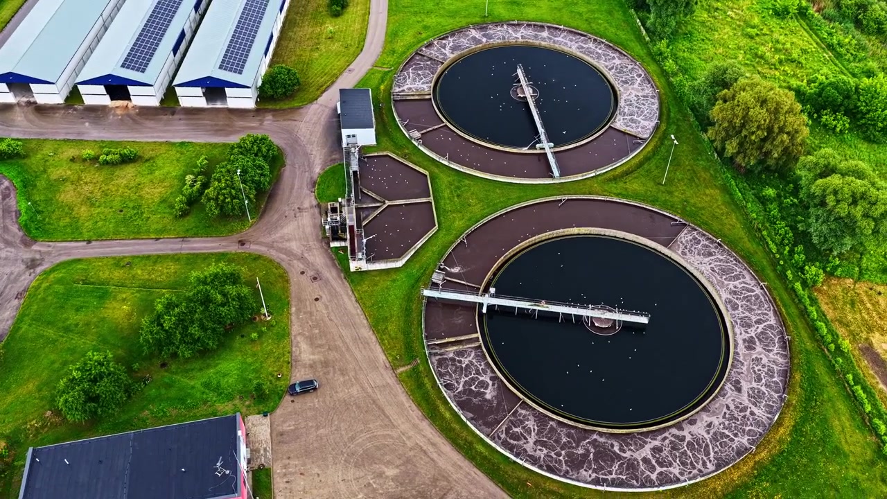 A Wastewater Treatment Facility With Large Circular Tanks Surrounded by Green Spaces and Service Roads - Aerial Drone Shot