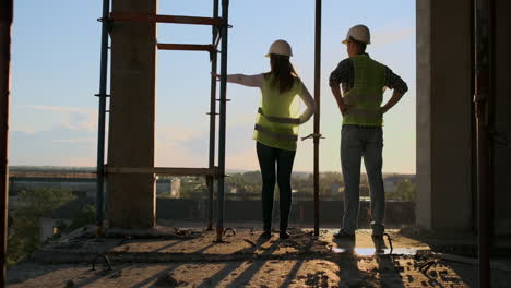vista trasera y lateral de un constructor caucásico con casco blanco y chaleco verde que parece un dibujo de pie sobre un fondo de construcción inacabada.