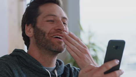 joven feliz teniendo video chat usando un teléfono inteligente hablando con un amigo soplando un beso disfrutando de la conversación en el teléfono móvil en casa