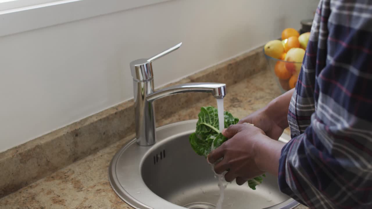homem sênior afro-americano em uma cozinha, lavando um repolho, distanciamento social e auto-isolamento