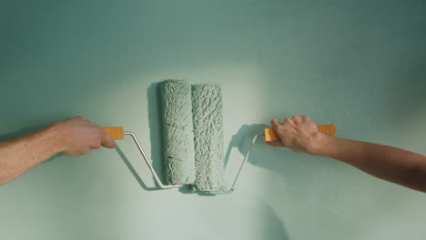 unknown couple doing decoration work in home. people pushing rollers on wall.