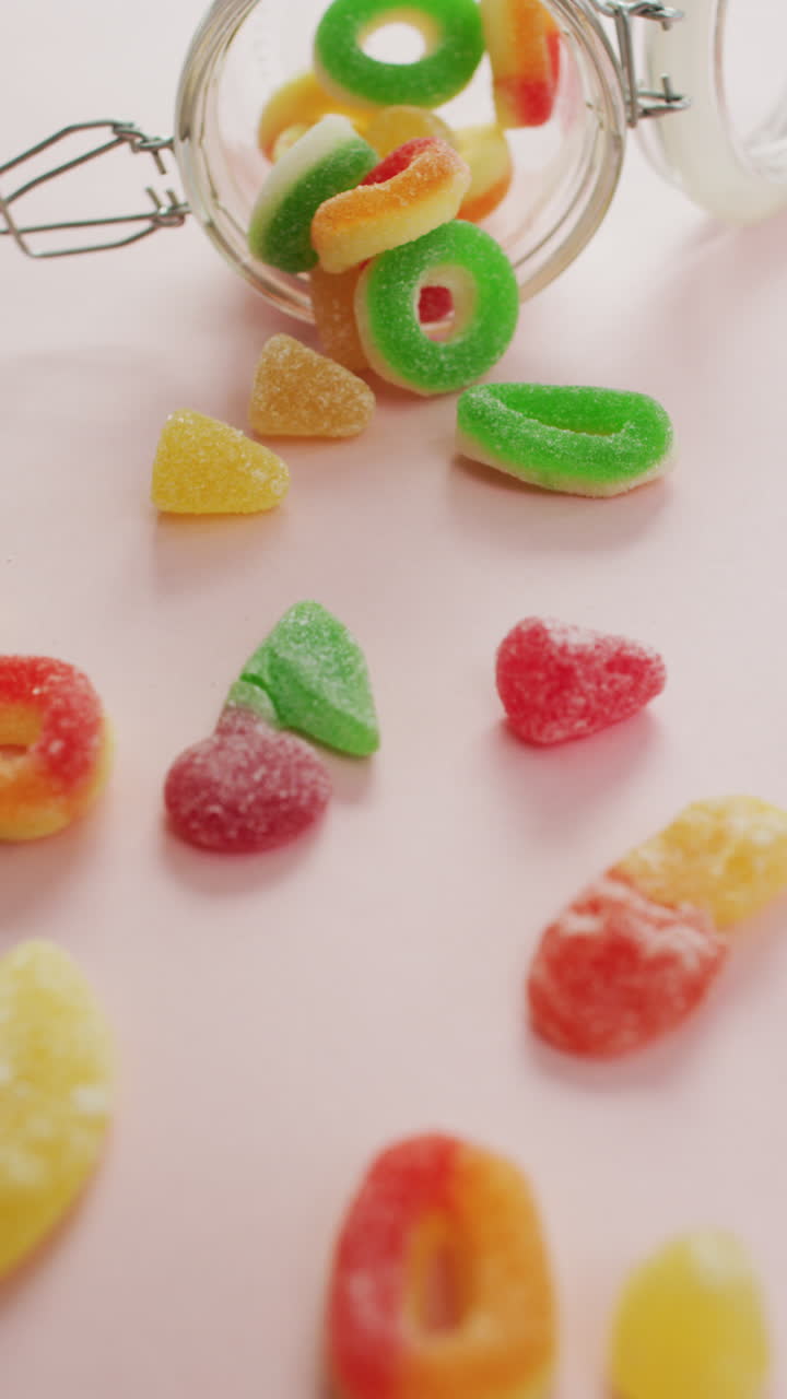 video vertical de caramelos de jalea que se derraman de un frasco de vidrio sobre un fondo rosado