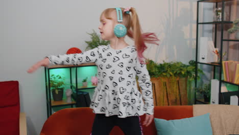 happy child girl kid in headphones dancing and jumping while listening to the music at home alone