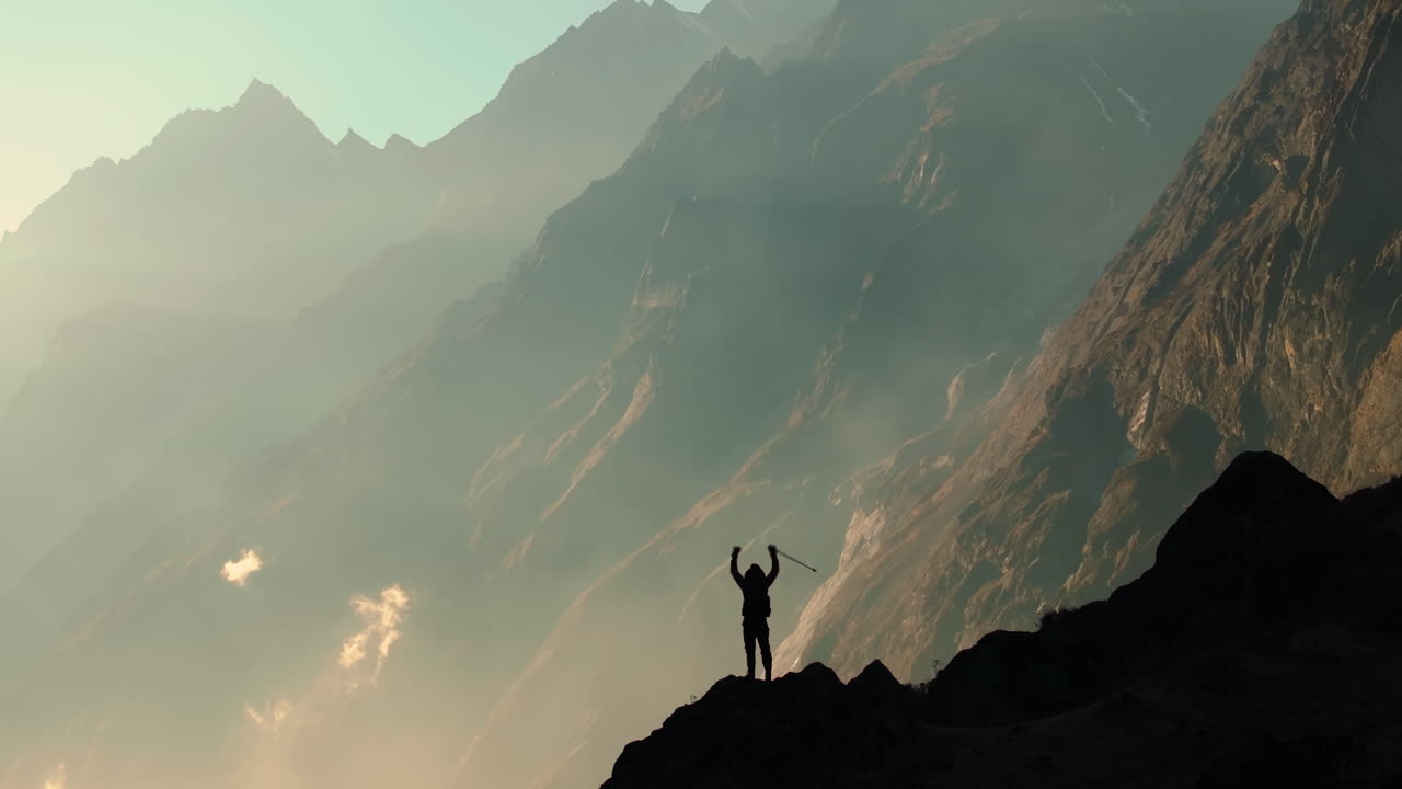 A gliding drone shot captures the silhouette of a male tourist entering the majestic landscape of snow-capped Himalayas in Langtang National Park, Nepal, during the golden hour of sunset.