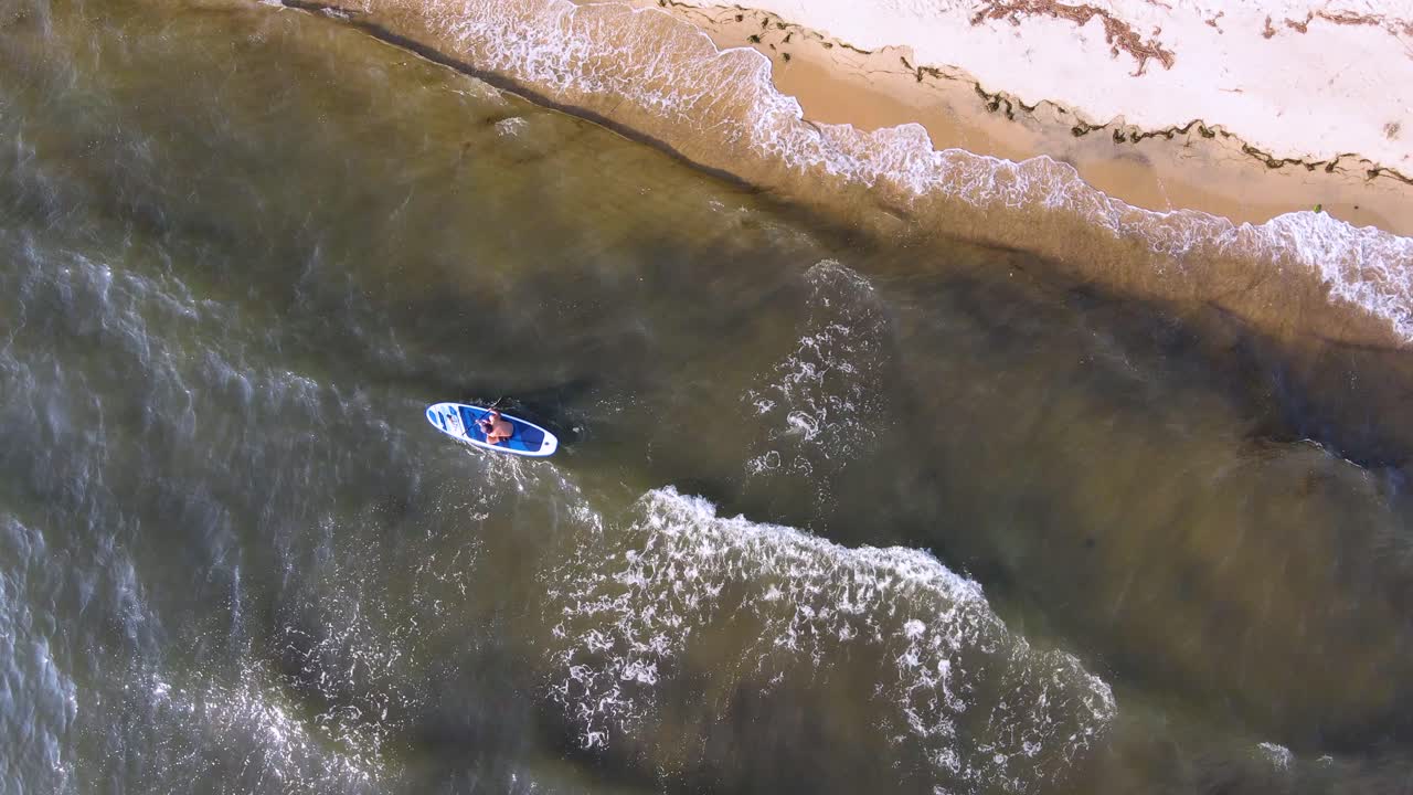 clip de arriba hacia abajo de una tabla de surf sup en las olas junto a una hermosa playa tropical