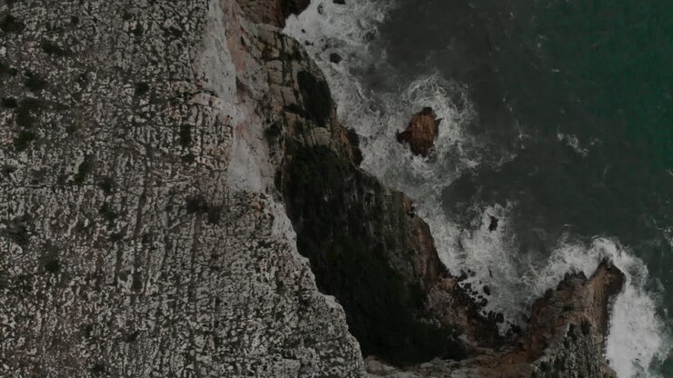 Vista aerea 4k di una scogliera rocciosa con onde e mare verde a Denia, Alicante, Spagna, ripresa grandangolare in allontanamento