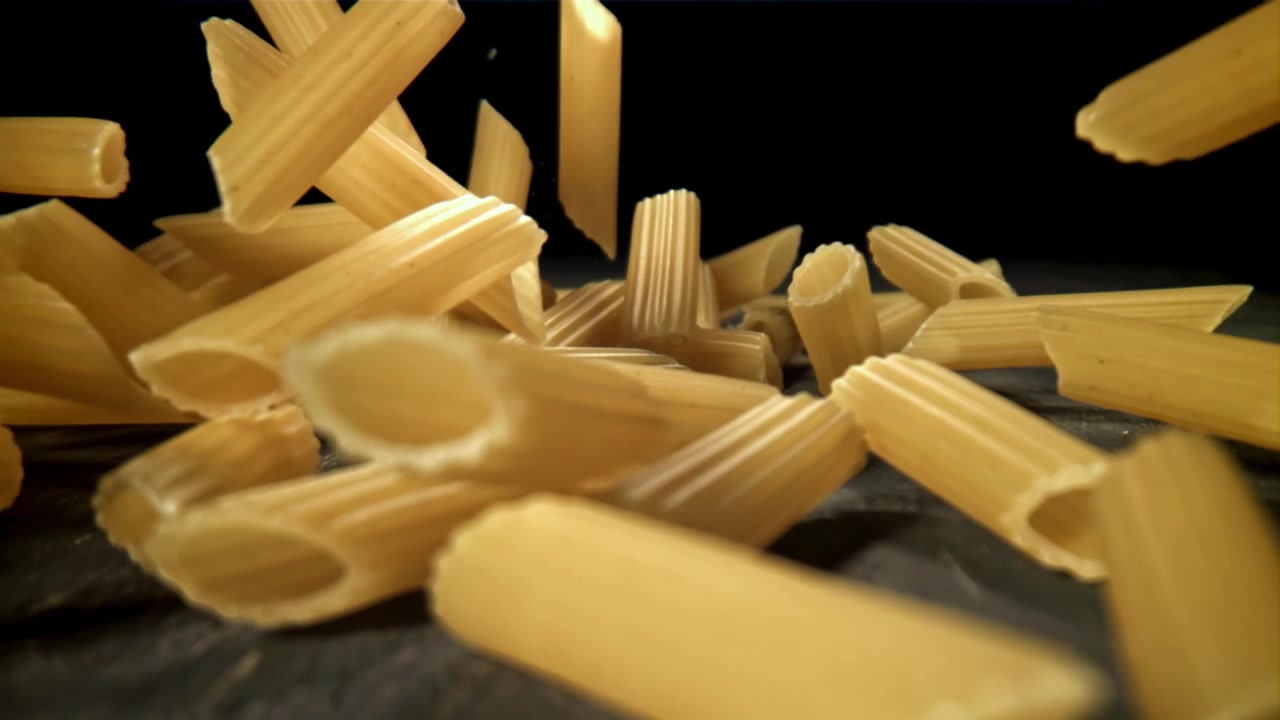 Penne secche che cadono al rallentatore su una superficie scura