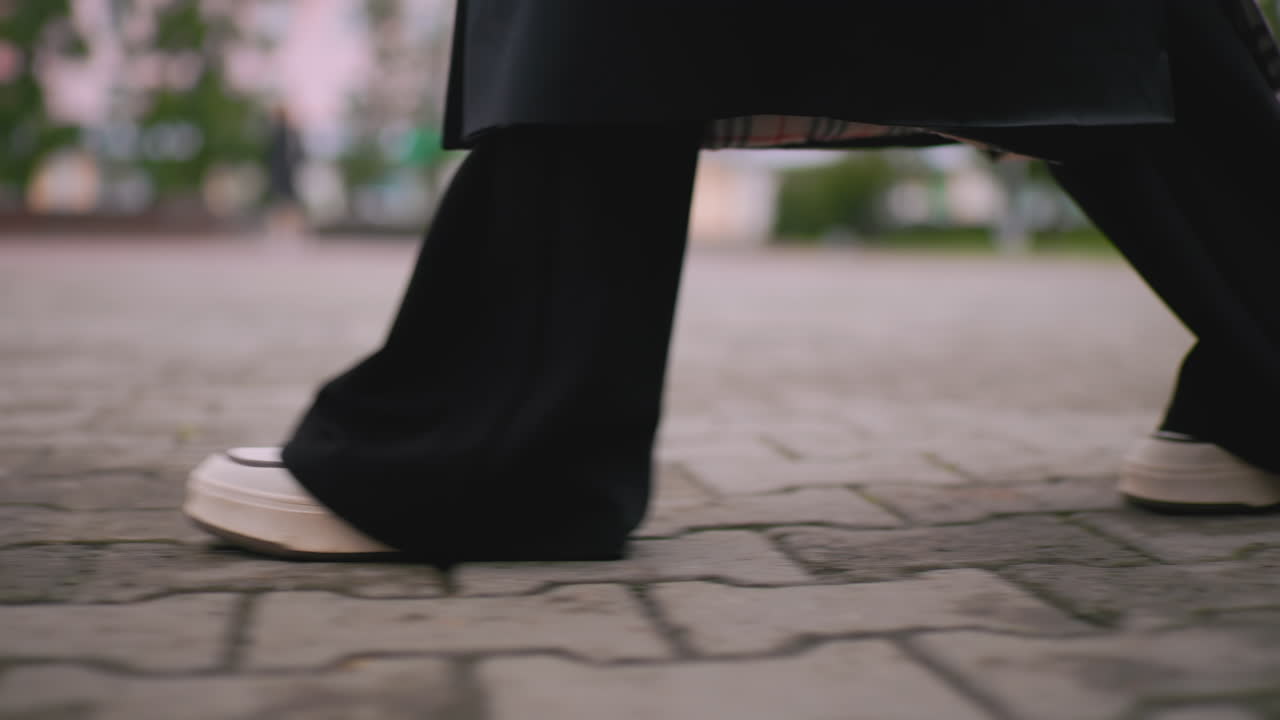 Close up of lady walking on stone pavement wearing black pants and white sneakers on cloudy rainy day, detail shot of steps in motion creating dynamic urban outdoor lifestyle with blurred background