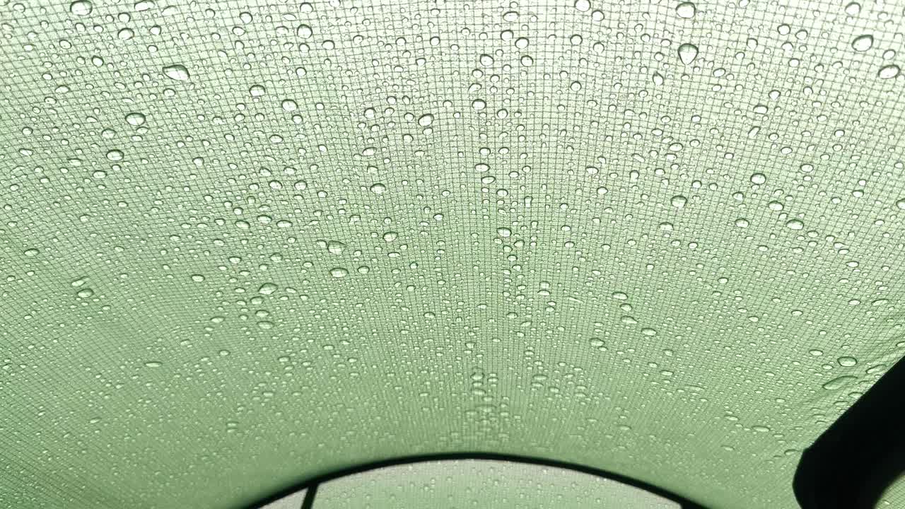 テントの中から見た内観。雨が生地に降り注いでいます。外からの雨粒がシェルター素材に当たり、雨中の質感、動き、保護を示しています。