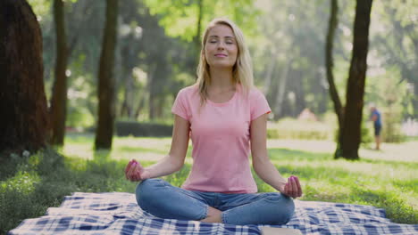 Glückliche-Frau-Praktiziert-Yoga-Und-Meditiert-In-Lotus-Pose,-Die-Draußen-Auf-Dem-Gras-Sitzt