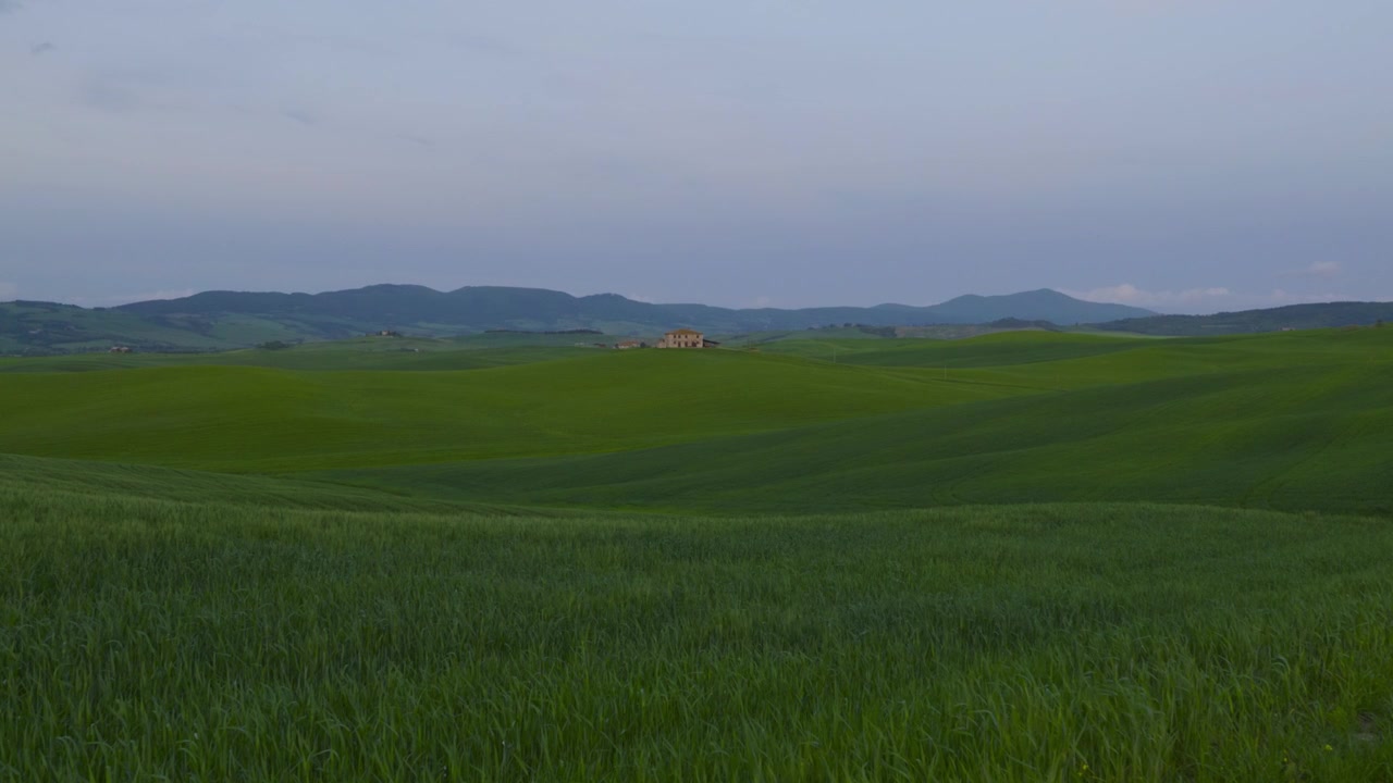 Breathtaking aerial view of the authentic Tuscany countryside featuring rolling green hills and a remote farmhouse under a soft twilight sky. Perfect for travel and wellness content.