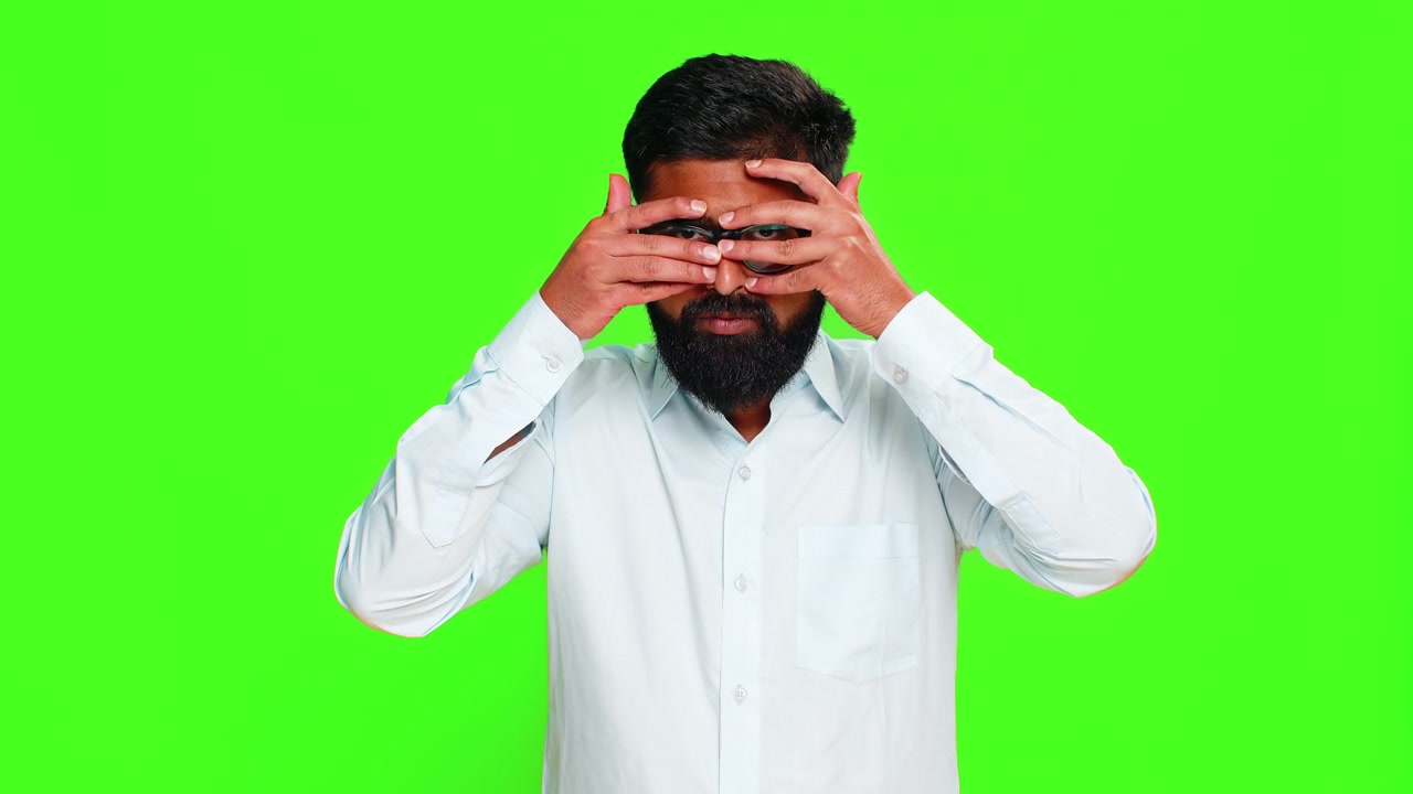 Homme indien se cachant un œil avec la main dans un geste d’espionnage montrant l’intrigue, le mystère, le secret, le regard, fond vert