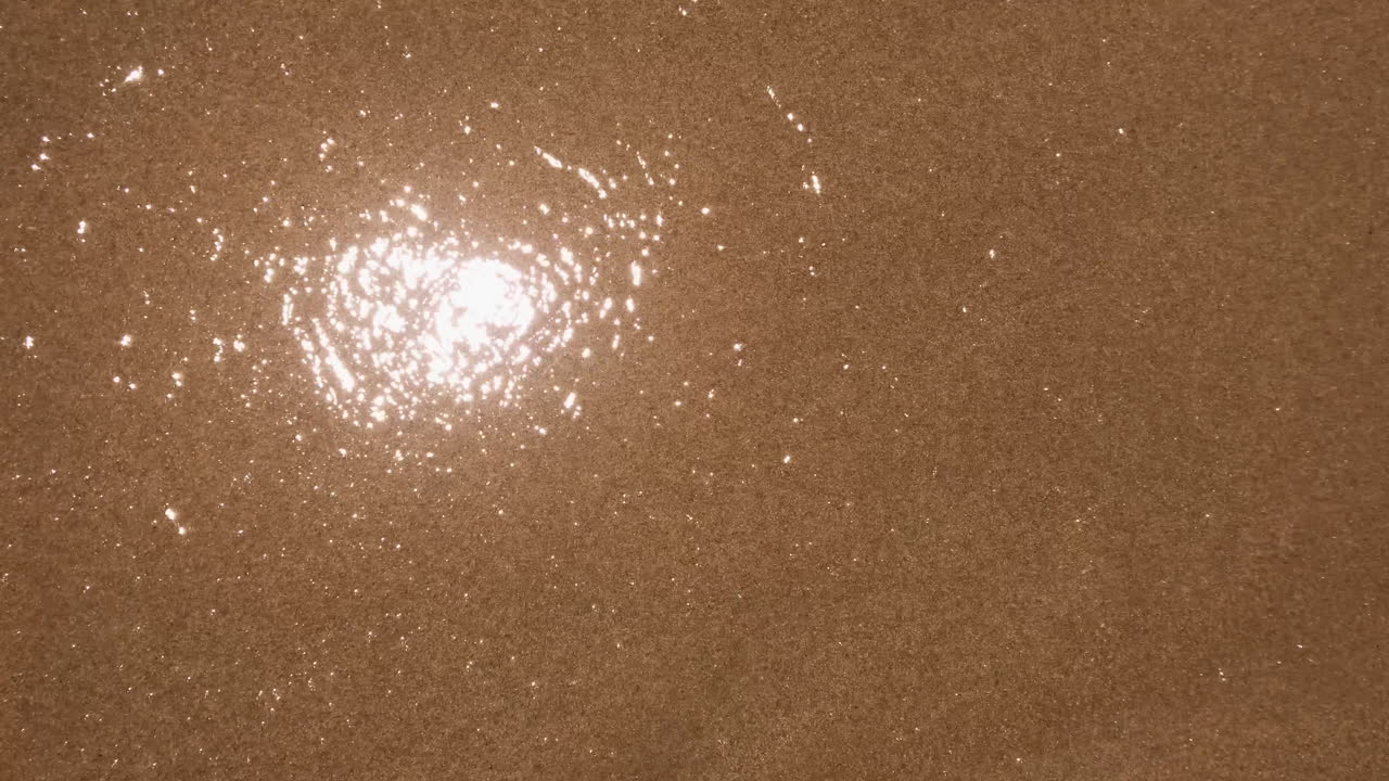 맑고 투명한 물이 갈색 모래 해변 표면 위로 빠르게 이동하고 오버헤드 정적 뷰를 닫습니다.