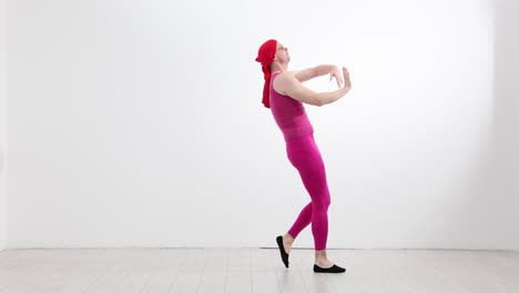 man in pink outfit and red headscarf performing expressive dance movements in a studio