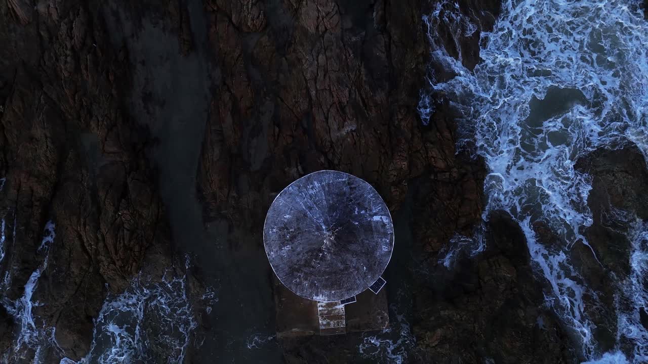Aerial view of a circular building on a rocky coast