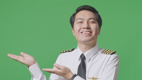 close up of asian man pilot smiling and pointing to side while standing in the green screen background studio